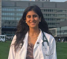  Photo of Isha smiling outdoors in a white coat with a stethoscope